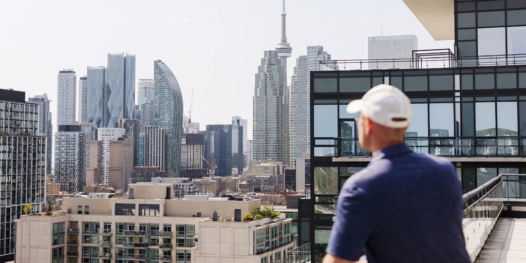 Man standing on a balcony overlooking downtown Toronto skyline with CN Tower