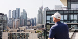 Man standing on a balcony overlooking downtown Toronto skyline with CN Tower