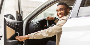Smiling man sitting in the driver’s seat of a car, holding the door open.