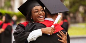 student loan repayment, graduates hugging during a graduation ceremony