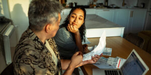 Couple reviewing household bills and finances together at a dining table in a home setting