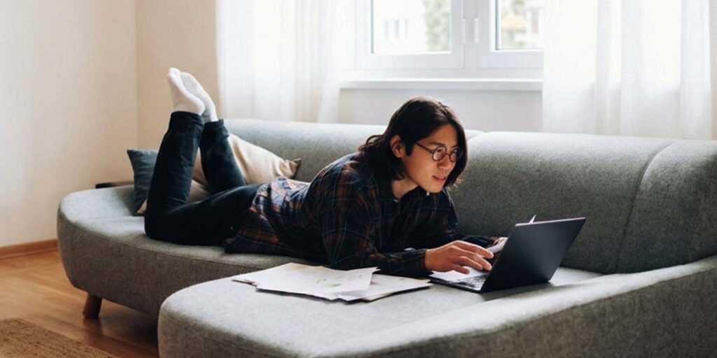 how to start investing in Canada, young person lying on couch reviewing financial documents on a laptop at home
