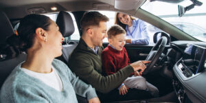 Family exploring a new car at a dealership while deciding between leasing and buying